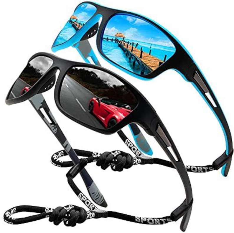 May include: Two pairs of sports sunglasses. One pair has a black frame with blue accents and mirrored lenses reflecting a beach scene. The other pair has a black frame with mirrored lenses reflecting a red car on a road. Both have black cords.