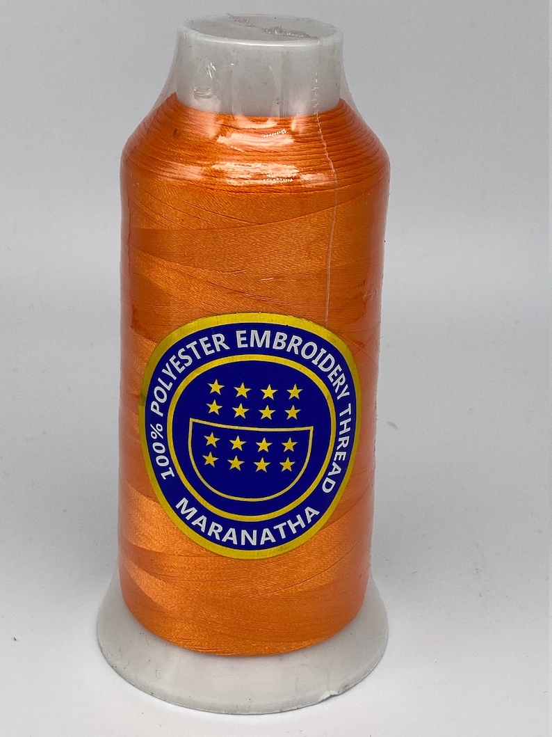 May include: A spool of orange embroidery thread with a white label that reads "100% Polyester Embroidery Thread Maranatha" with a blue circle containing stars.