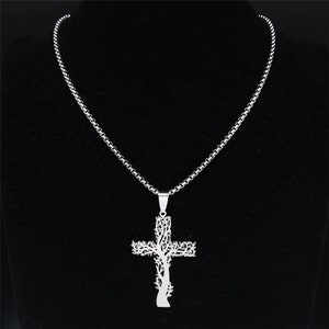 May include: A silver chain necklace with a pendant in the shape of a cross. The cross is made of a tree design with intricate details.