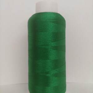 May include: A spool of bright green thread on a white plastic bobbin. The thread is wound tightly and has a smooth, shiny finish.