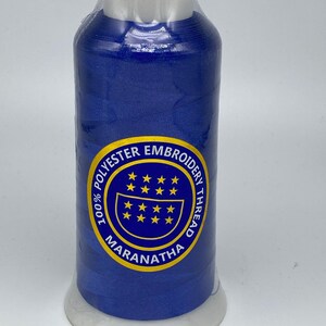May include: A spool of 100% polyester embroidery thread in a vibrant blue color. The spool has a white label with the text "100% POLYESTER EMBROIDERY THREAD MARANATHA" in a blue circle with yellow stars.
