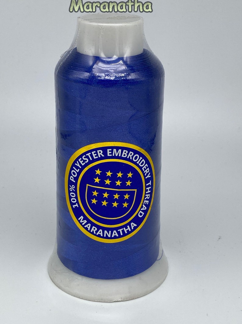 May include: A spool of 100% polyester embroidery thread in a vibrant blue color. The spool has a white label with the text "100% POLYESTER EMBROIDERY THREAD MARANATHA" in a blue circle with yellow stars.
