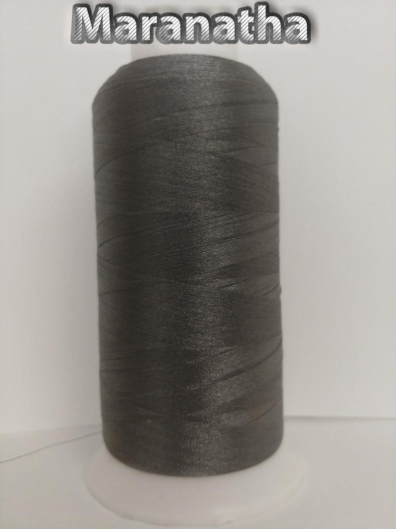 May include: A spool of dark gray thread on a white bobbin. The spool is labeled "Maranatha".