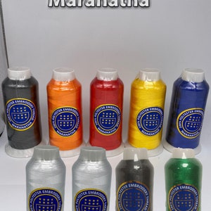 May include: Assortment of 10 spools of embroidery thread in various colors, including black, orange, red, yellow, blue, silver, green, and gray. Each spool has a label that reads "100% Polyester Embroidery Thread" and "Maranatha".