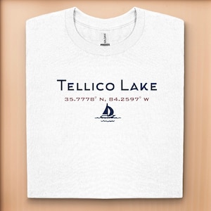 May include: White t-shirt with a navy blue graphic that says "Telllico Lake" and the coordinates "35.7778° N, 84.2597° W". A small sailboat graphic is below the text.