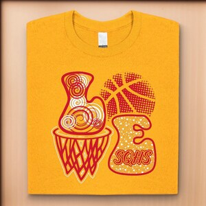 May include: A yellow t-shirt with a red and white graphic design of a basketball hoop, basketball, and the letters "LOVE" with the text "SQHS" inside the letter "E".