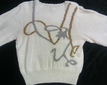 May include: White knitted sweater with a gold and silver design. The design is a stylized image of a pair of skis and a skier.