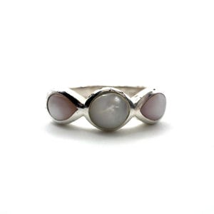 May include: A silver ring featuring three gemstones. The center stone is a light gray, round shape, flanked by two teardrop-shaped, pale pink stones. The ring has a simple, elegant design.