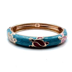 May include: A rose gold hinged bangle bracelet with a turquoise enamel finish. The bracelet features turtle designs in white, pink, and red. The bracelet is approximately 2.5 inches in diameter.