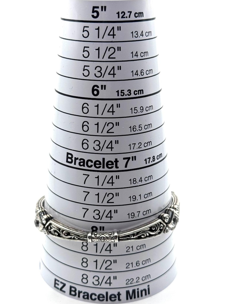 May include: A silver bracelet with an ornate design is placed on a white EZ Bracelet Mini sizer. The sizer shows measurements in inches and centimeters, with the bracelet fitting at approximately 7 inches (17.8 cm).