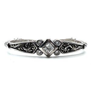 May include: A silver bracelet with an ornate design. The bracelet features a central square-cut clear stone, surrounded by smaller round stones. The band has a detailed, swirling pattern. A classic piece of jewelry.