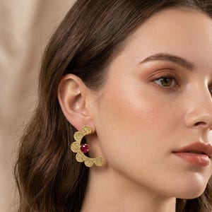 Puede incluir: Pendientes dorados texturizados con forma de media luna y borde festoneado. Cada pendiente presenta una pequeña gema roja redonda. Estos pendientes son una pieza llamativa, que añade un toque de elegancia.
