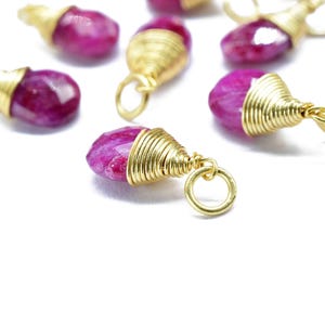 Peut inclure: Gros plan de plusieurs pendentifs en pierres précieuses rubis avec un fil d'or et de petites boucles dorées. Les rubis facettés en forme de goutte d'eau sont d'une couleur rose-rouge vif. Le fil d'or est enroulé autour du haut de chaque pierre.