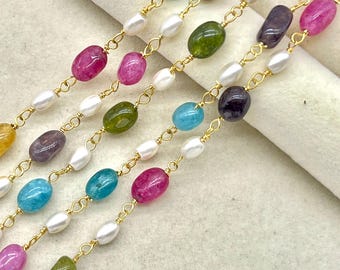 Puede incluir: Primer plano de varias hebras de collares con cadenas doradas. Cada hebra presenta una combinación de perlas blancas y piedras preciosas ovaladas de colores en tonos rosa, verde, azul y morado. Los collares se muestran sobre un fondo neutro.