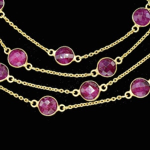 Puede incluir: Primer plano de múltiples hilos de collares dorados con piedras preciosas redondas, facetadas, de color rubí. Los collares se colocan sobre un fondo negro, resaltando el diseño y el color de la joyería.