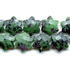 May include: Strand of star-shaped beads. Each bead is faceted and features a mix of green, black, and purple hues. The beads are strung on a thin, silver-colored wire, creating a decorative element.