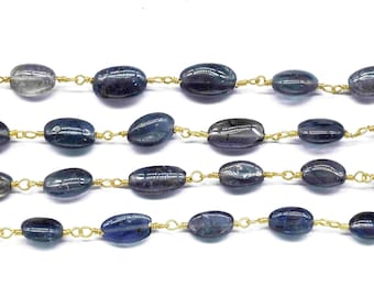 May include: Close-up of several strands of blue-grey oval gemstones strung on delicate gold-colored wire. The gemstones have a polished, smooth surface and vary slightly in color. The background is plain white, highlighting the jewelry.