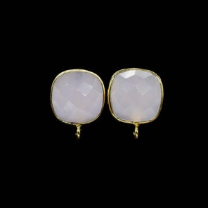 May include: A pair of square earrings featuring pale pink, faceted gemstones, set in gold-coloured metal. Each earring has a small loop at the base. The background is a plain black.