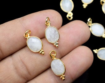 May include: Gold-toned oval pendants with a white, iridescent stone center. Each pendant has a small loop at the top and a decorative cluster at the bottom. The pendants are displayed against a dark background.