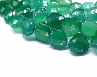 Puede incluir: Primer plano de una colección de piedras preciosas verdes facetadas en forma de lágrima. Las gemas son de un color verde intenso y vibrante y parecen pulidas. Las piedras preciosas están dispuestas sobre una superficie blanca, creando un contraste.