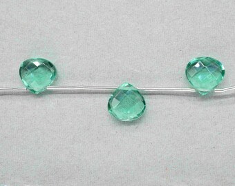 Op de afbeelding: Drie gefacetteerde, druppelvormige kralen in een lichtblauwe kleur zijn geregen op een dun, zilverkleurig draadje. De kralen hebben een geslepen glazen uiterlijk en reflecteren licht. De kralen worden gepresenteerd tegen een lichtgrijze achtergrond, wat wijst op een thema van sieraden maken.