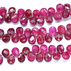May include: Close-up of strands of faceted, teardrop-shaped ruby beads. The beads are a deep, rich pink and red hue, with multiple facets catching the light. The beads are strung together, creating a beautiful display of color and texture.