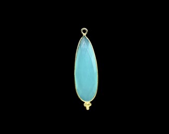 May include: A teardrop-shaped pendant with a light blue gemstone, framed in gold. The pendant has a faceted surface and a small gold loop at the top for hanging. A small gold accent is at the bottom.