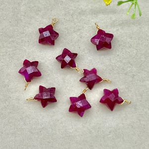 以下が含まれることがあります： 深紅色のファセット加工された星型の宝石のクローズアップ。各星は金色のワイヤーで個別に配線され、一部はチェーンで接続されています。宝石は明るい色の表面に配置されています。