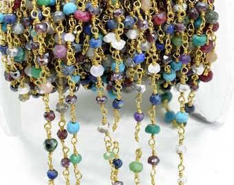 May include: A spool of gold-toned wire-wrapped chain featuring a variety of multi-colored, faceted gemstone beads. The beads include shades of blue, red, green, and white, individually linked by thin gold-colored metal wire segments.