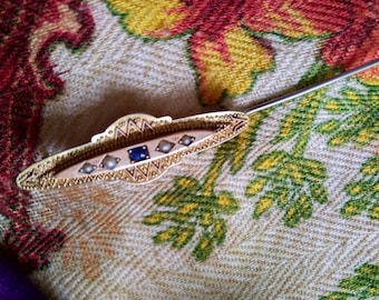 Könnte beinhalten: Eine goldfarbene Brosche mit einem Design aus blauen und weißen Steinen. Die Brosche ist mit Perlen besetzt und hat ein filigranes Muster.