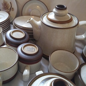 Puede incluir: Una colección de tazas de té y una tetera de cerámica marrón y blanca con un esmalte moteado. La tetera tiene un asa marrón y un borde marrón. Las tazas de té tienen bordes marrones y asas marrones. Las tazas de té tienen un esmalte moteado marrón y blanco.