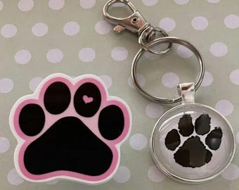 May include: A pink and black paw print-shaped magnet with a small pink heart, a silver keychain with a paw print pendant, and a silver clasp. The items are on a light green background with white polka dots.