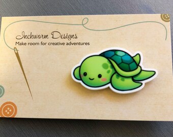 May include: A green and blue cartoon turtle with a smiling face. The turtle is on a card with the text "Inchworm Designs Make room for creative adventures".