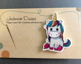 May include: A white unicorn with a rainbow mane and tail, sitting on a brown background with the text "Inchworm Designs Make room for creative adventures".