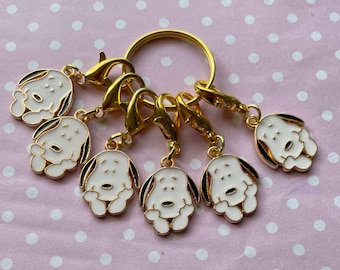 May include: A gold key chain with six charms featuring cartoon dogs with black eyes and white bodies. The charms are attached to a gold ring.