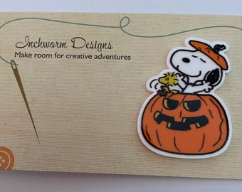 May include: Snoopy and Woodstock are sitting inside a jack-o'-lantern pumpkin. Snoopy is wearing a red and white hat. The image is on a brown background with the text "Inchworm Designs Make room for creative adventures".