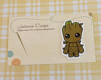 May include: A Groot character sticker on a cream-colored card with the text "Inchworm Designs" and "Make room for creative adventures". The background is a yellow plaid pattern.