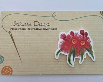 May include: A business card with the text "Inchworm Designs" and the tagline "Make room for creative adventures". A needle and thread are shown in the background. A pink and green floral design is on the card.