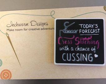 May include: A magnet with the text "TODAY'S FORECAST Cross Stitching with a chance of CUSSING" on a black background. The magnet is on a light brown background with the text "Inchworm Designs" and a needle and thread design.
