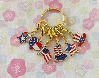 May include: A gold keyring with six charms in patriotic designs. Charms include a star, a heart, an American flag, a cowboy boot, a star with stripes, and a Uncle Sam hat. The charms are red, white, and blue.