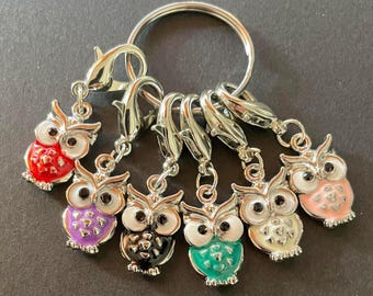 May include: A collection of seven owl-shaped charms in various colors, including red, purple, black, teal, white, and pink, attached to silver-tone lobster clasps and a large metal ring. The charms have black eyes and white accents.