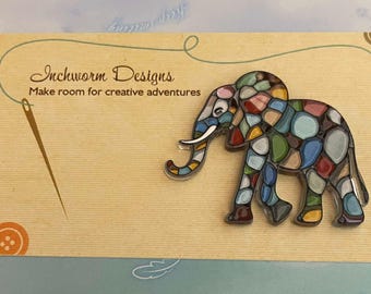 May include: A colourful mosaic elephant pin with a blue, green, yellow, red and white design. The pin is on a card that says "Inchworm Designs" and "Make room for creative adventures".