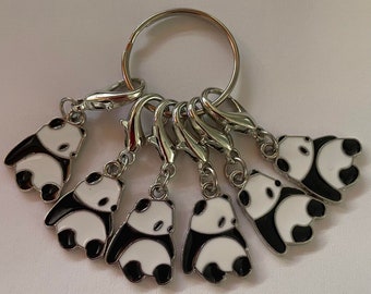 May include: A set of seven silver panda charm keyrings. Each charm features a black and white panda bear design. The keyrings are attached to a silver ring.