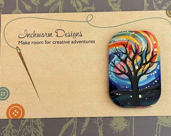 May include: A colourful, hand-painted ceramic tag with a whimsical tree design. The tag features a black silhouette of a tree with branches against a background of swirling rainbow colours and white dots. The tag is labelled "Inchworm Designs" and "Make room for creative adventures".