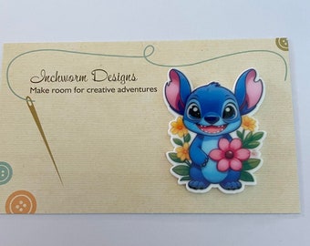 May include: Blue Stitch character holding a pink flower with yellow flowers and green leaves around it. The character is on a beige background with the text "Inchworm Designs Make room for creative adventures".