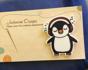 May include: A white penguin with black wings and a red headband with headphones on, listening to music. The penguin is on a beige background with the text "Inchworm Designs Make room for creative adventures".
