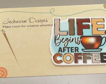May include: A sticker with the text "LIFE Begins AFTER COFFEE" in brown, tan, and blue colors, with a coffee cup graphic. The sticker is on a tan card with the text "Inchworm Designs" and a needle and thread design.