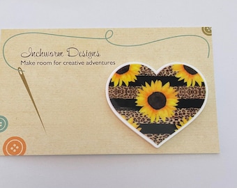 May include: A heart-shaped decorative item with a sunflower design and black and leopard print stripes. The item is on a tan card with the text "Inchworm Designs" and "Make room for creative adventures".