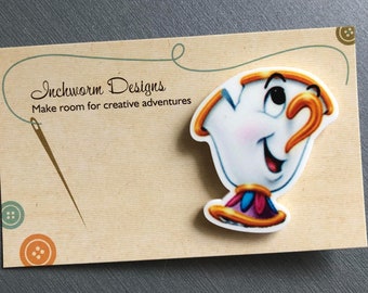 May include: A Chip character-shaped sticker with a smiling face, featuring a white body, gold handle and rim, and a colorful base. The sticker is on a tan card with the text "Inchworm Designs" and "Make room for creative adventures."