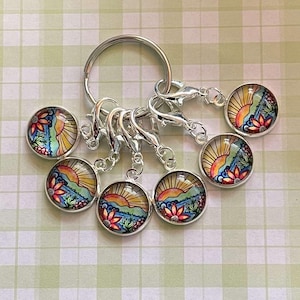 Può includere: Un set di sei marcatori di punto colorati con un design di tramonto e fiori. I marcatori sono attaccati a un portachiavi argentato.